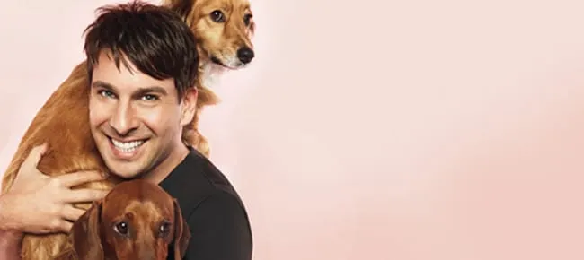Celebrity Peter Alexander smiling while holding his beloved dachshund Penny and a fluffy dog.