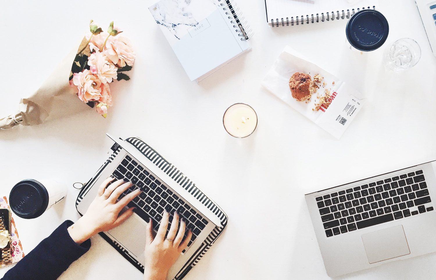 Hands typing on a laptop at a desk with flowers and coffee for Pretty Fluffy advertising and general enquiries.