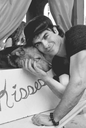 Black and white lifestyle photography of Ian Somerhalder cuddling a dog at a kissing booth.