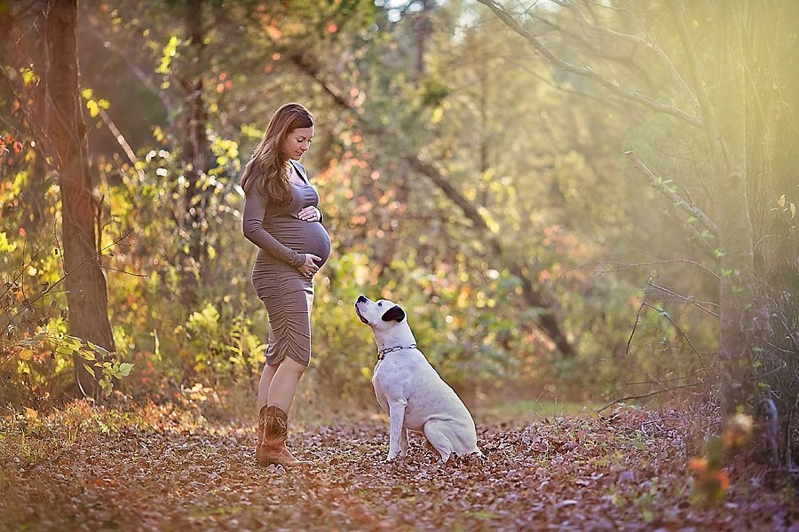 Pregnant woman and white dog in a wooded area for a dog-friendly maternity session by April Ziegler Photography.