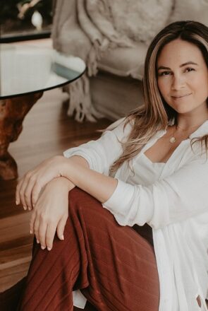 Sonia Bavistock of Scribe+Social sits in her modern living room with a white sofa and wood coffee table for a home tour.