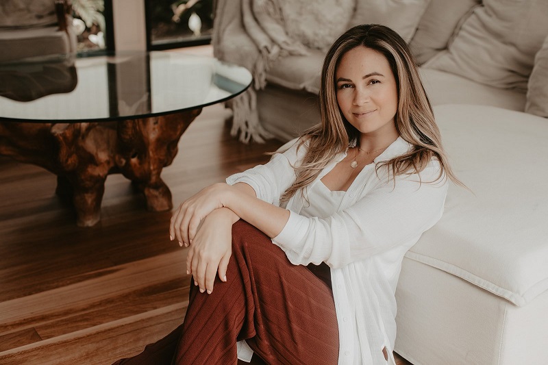 Sonia Bavistock of Scribe+Social sits in her modern living room with a white sofa and wood coffee table for a home tour.