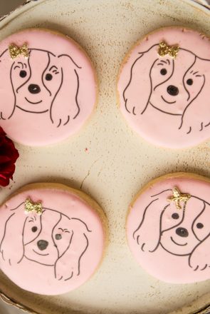 Pink sugar cookies with spaniel dog illustrations and gold bows on a platter for a dog lovers meetup party.
