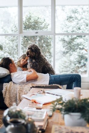 Couple relaxing on a sofa with their fluffy brown dog during a candid in-home pet photo shoot in a bright living room.