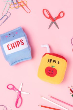 Cute plush dog toys shaped like a chip bag and apple juice box on a pink background, featured in editor’s picks.