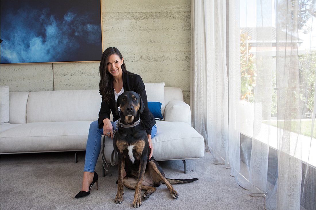 Molly Barker of Melbourne designer dog boutique sitting on a white couch with her large black and tan dog.