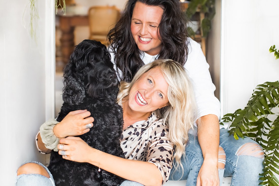 New Pretty Fluffy editors smiling and hugging a fluffy black dog for their pet lifestyle blog.