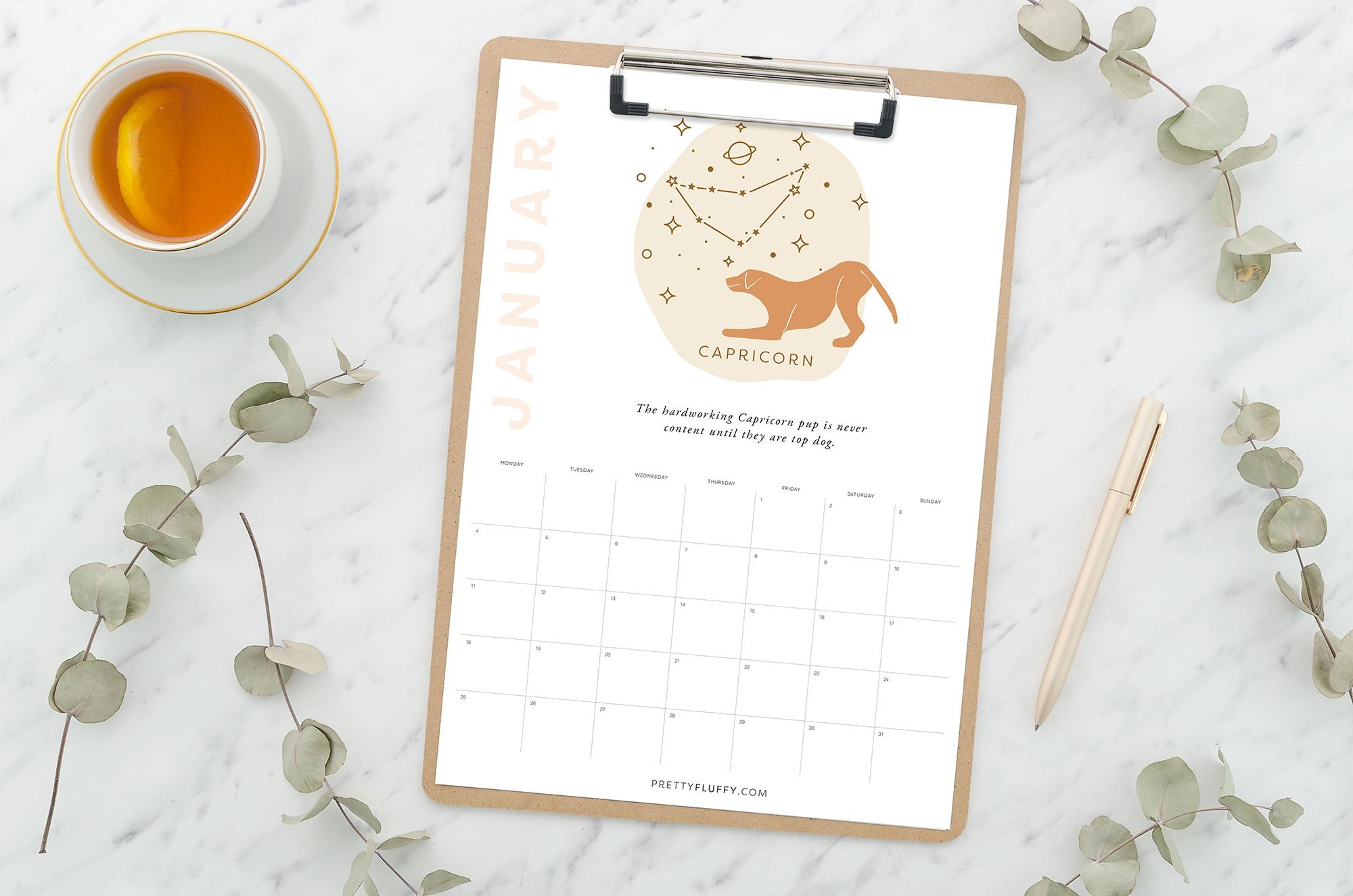 Printable January 2021 dog zodiac calendar for Capricorn on a clipboard with tea and eucalyptus branches.