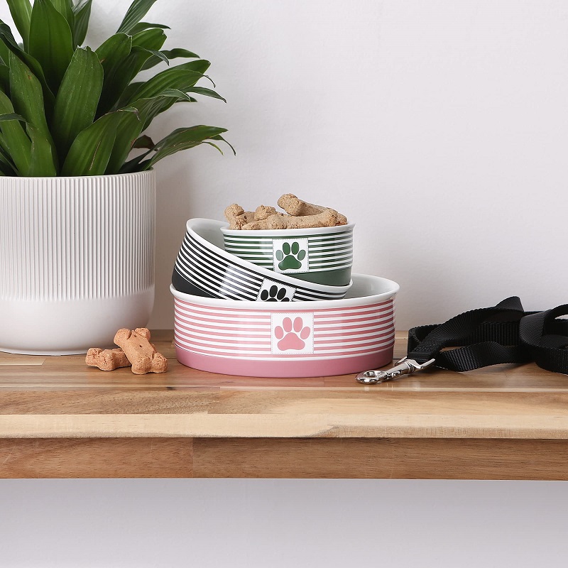 Stacked ceramic dog bowls with stripes and paw prints, featuring bone treats and a dog leash on a wooden table.