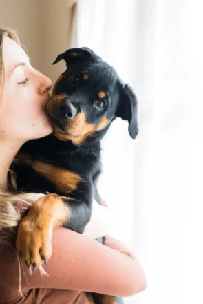Woman kissing a Rottweiler puppy on the cheek to show how to bond with your puppy through affection.