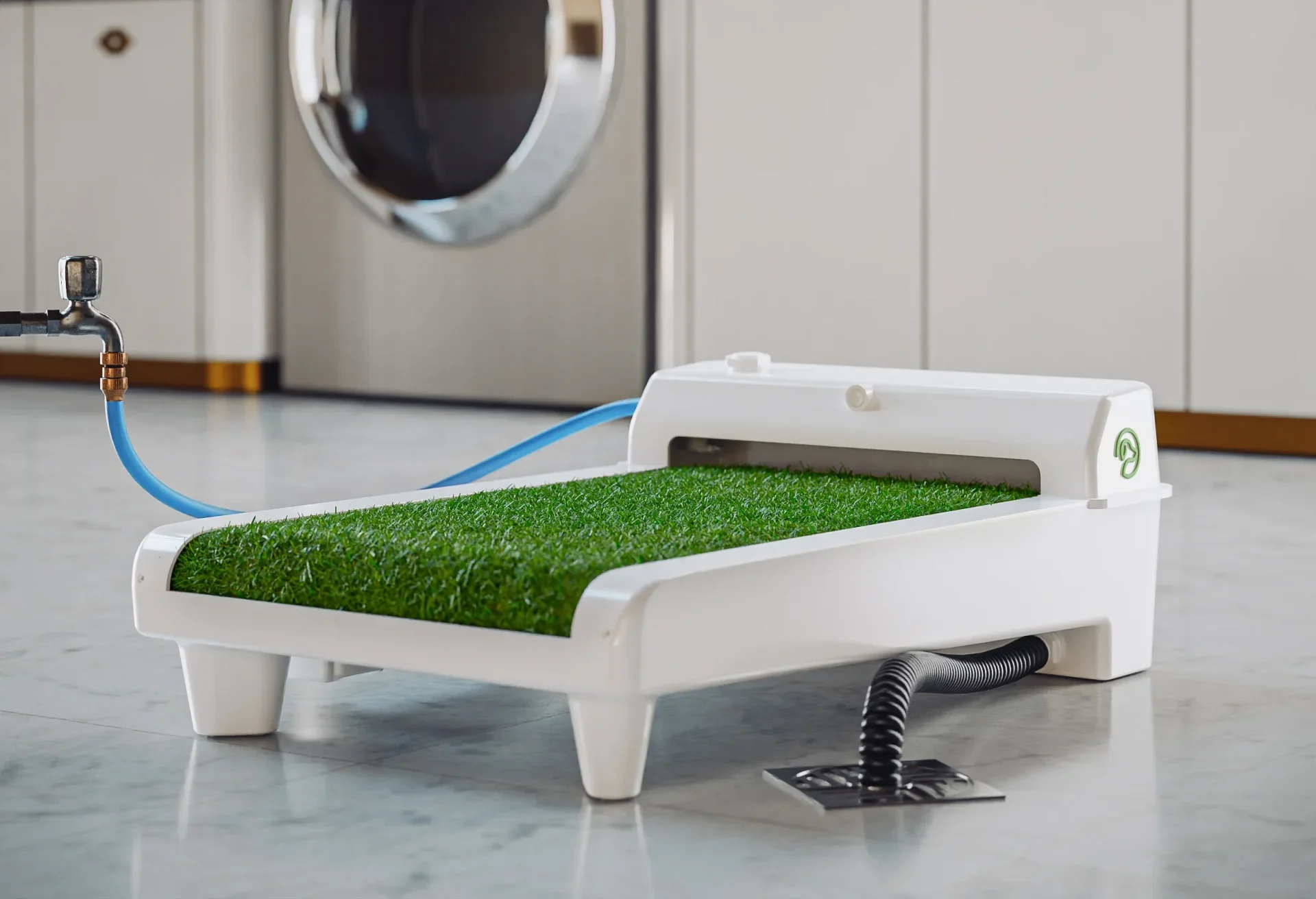 Fydoo self-cleaning dog toilet with artificial grass connected to a water tap and drain in a laundry room.