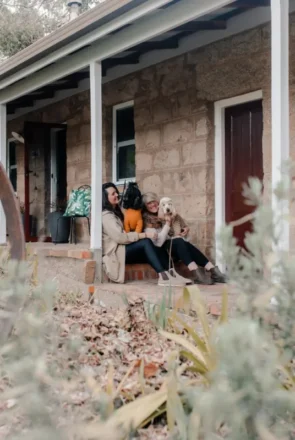 Two people with dogs sitting on the stone porch of Granite Cottage, pet-friendly accommodation in Beechworth.