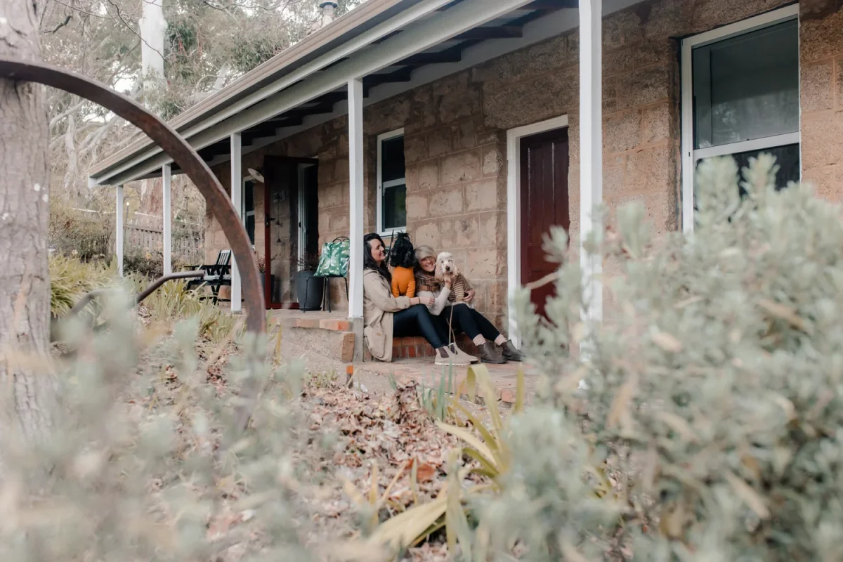 Two people with dogs sitting on the stone porch of Granite Cottage, pet-friendly accommodation in Beechworth.