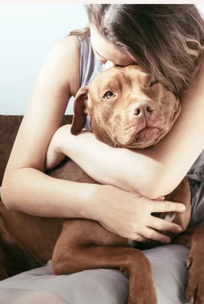 Woman hugging her brown dog, illustrating the emotional health and wellbeing benefits of pet companionship.