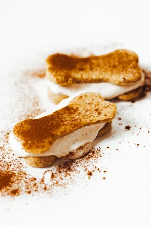 Healthy homemade dog treat recipe: bone-shaped cookie sandwiches with cream filling and cinnamon dusting.