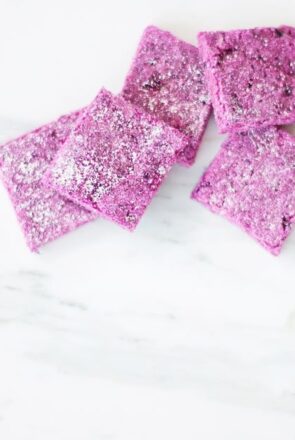 Square-cut pink banana and beetroot dog treats on a white marble surface from a DIY dog treat recipe.